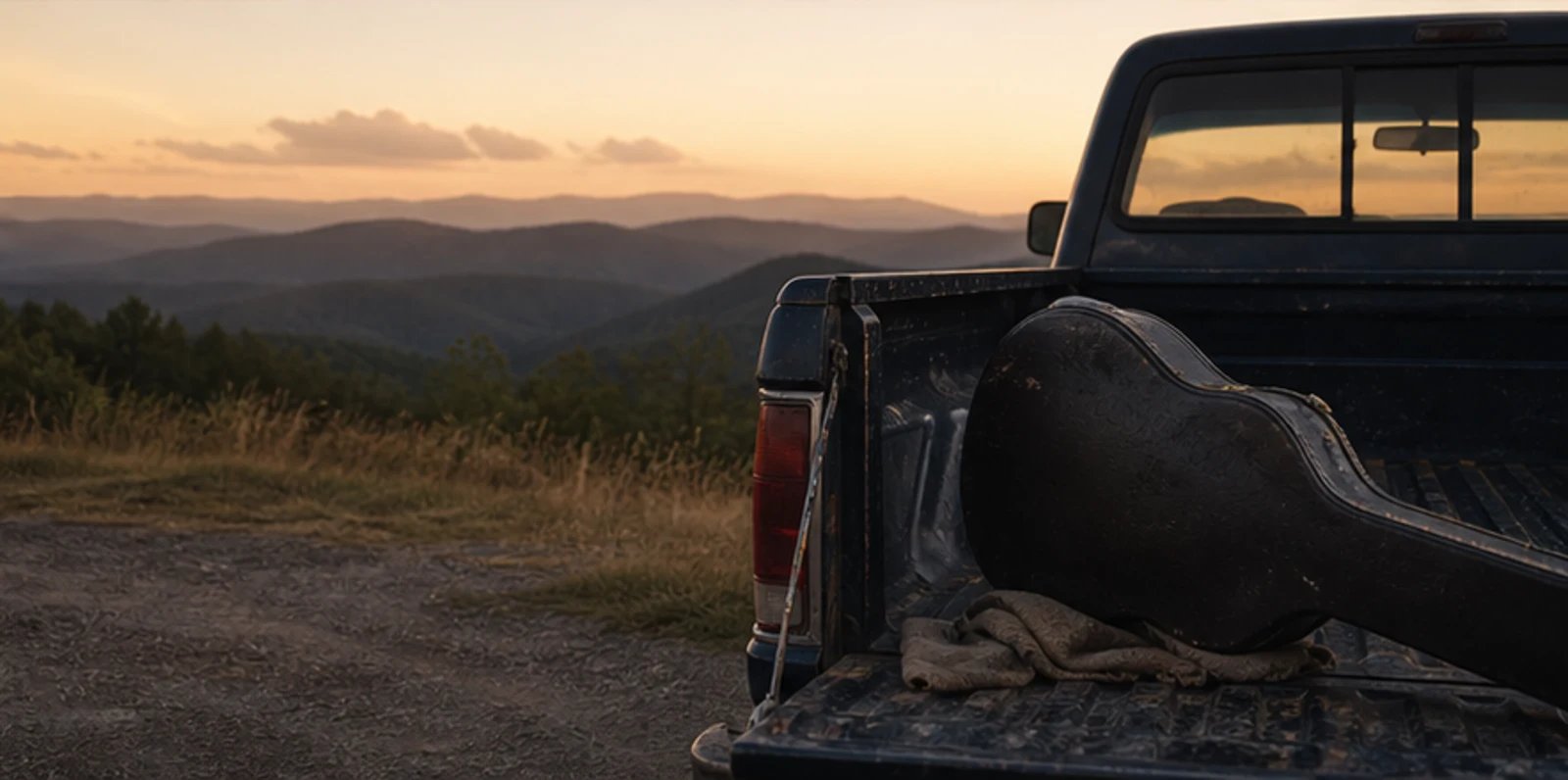 Pickup truck tailgate with a guitar case overlooking mountains at golden hour